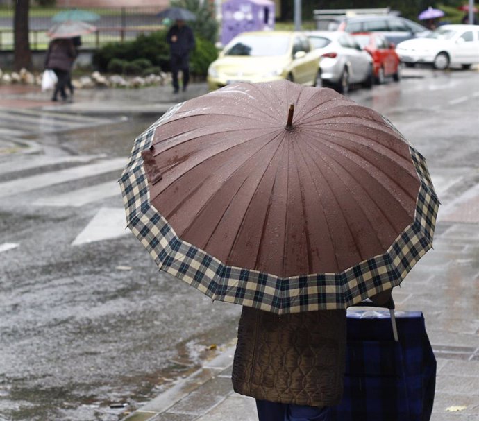 Archivo - Una mujer pasea bajo su paraguas al frescor que la lluvia le ha dejado. 