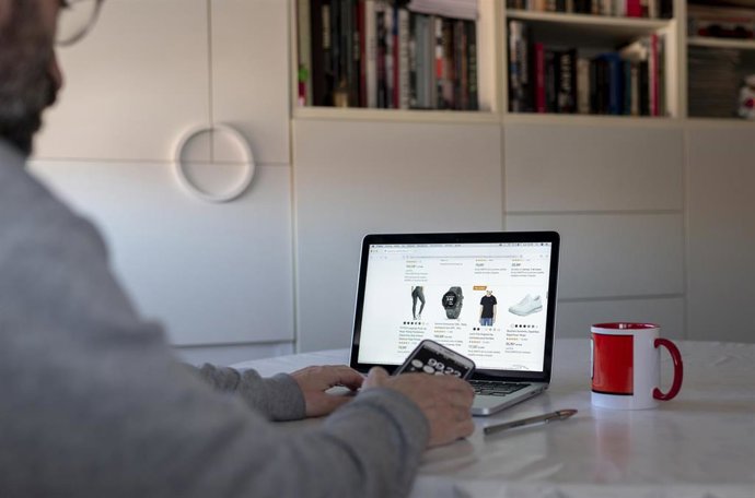 Archivo - Una persona compra con su teléfono móvil y ordenador.