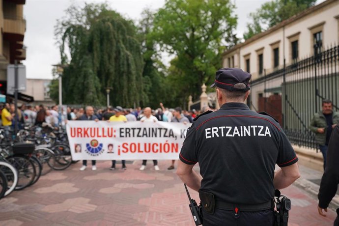Archivo - Un ertzaina frente a varias personas que sostienen una pancarta que reza: 'Urkullu: Ertzaintza, Konponbidea! ¡Solución ya!' durante una manifestación de la Unidad de Acción Sindical de la Ertzaintza (ErNE-ESAN- SIPE- Euspel), a 27 de junio de 