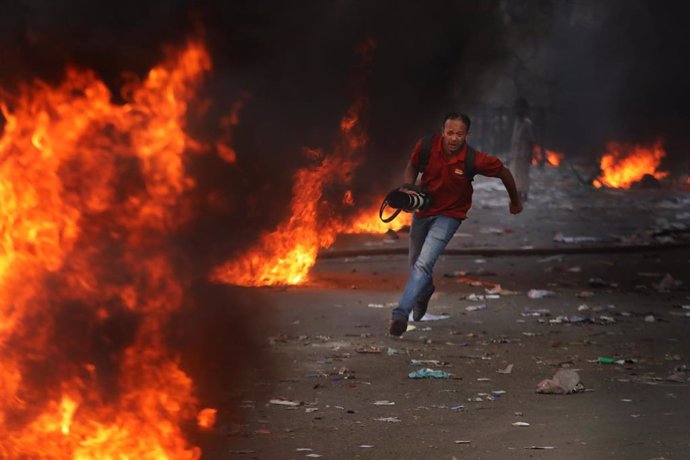 Un fotógrafo se pone a cubierto durante las protestas en Dacca contra el Gobierno de Bangladesh