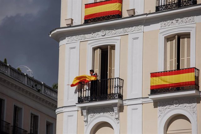 Una persona coloca una bandera de España en su balcón durante los preparativos del acto para la jura de la Constitución de la Princesa Leonor