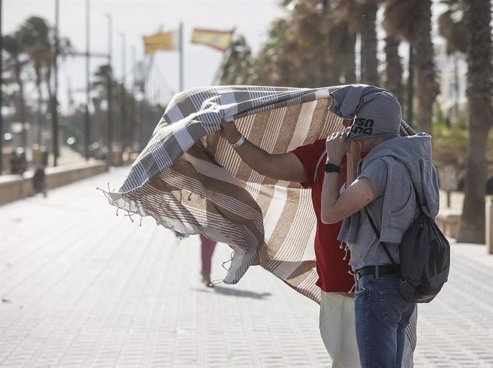Dos personas se refugian del viento en el paseo de la playa de la Malvarrosa de València