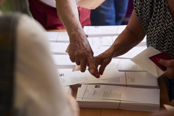 Archivo - Varias personas cogen votos de una mesa electoral, en imagen de archivo