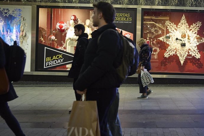 Archivo - Varias personas pasan por delante de los comercios que anuncian los descuentos del Black Friday 