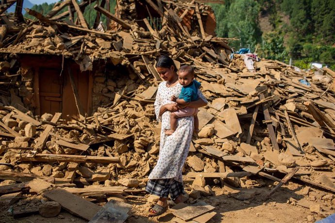 Una mujer y su hijo paseando junto a una casa destruida por un terremoto en Nepal