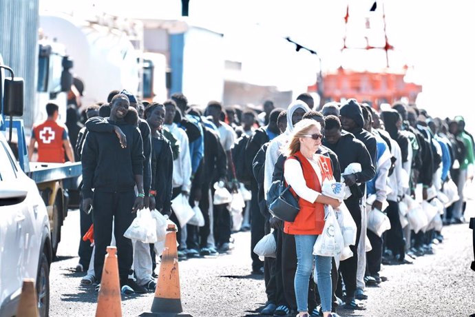 Una voluntaria de Cruz Roja al lado de decenas de migrantes antes de subir a un ferry hacia Tenerife desde El Hierro, a 3 de noviembre de 2023, en El Hierro, Santa Cruz de Tenerife, Canarias (España). Un segundo cayuco con unos 70 migrantes a bordo ha l