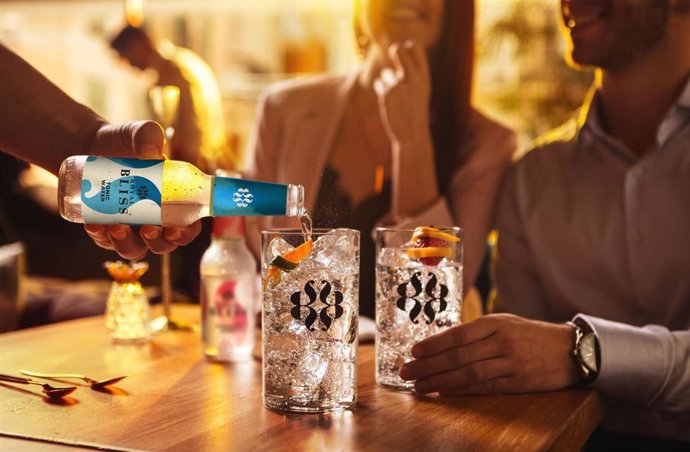 Una persona sirve a dos comensales una bebida en un bar.