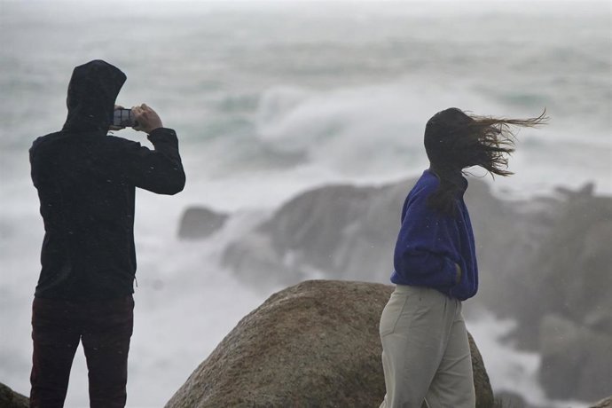 Una persona fotografía el mar embravecido, mientras el viento mueve la melena a su acompañante, a 4 de noviembre de 2023, en A Coruña, Galicia (España). La Agencia Estatal de Meteorología (AEMET) ha activado en A Coruña el aviso rojo por la llegada de l