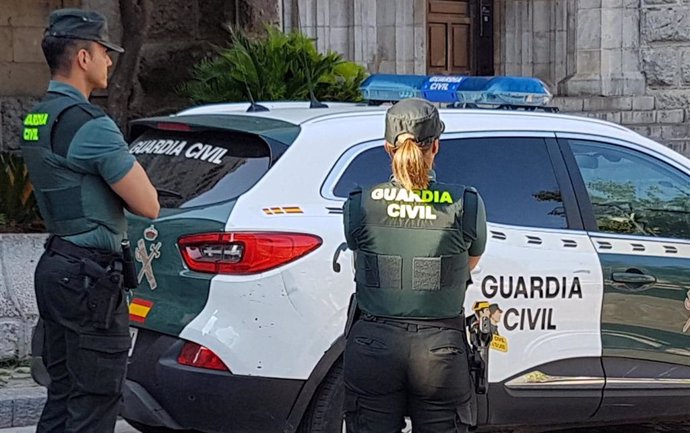 Archivo - Dos guardias civiles ante un vehículo del cuerpo.