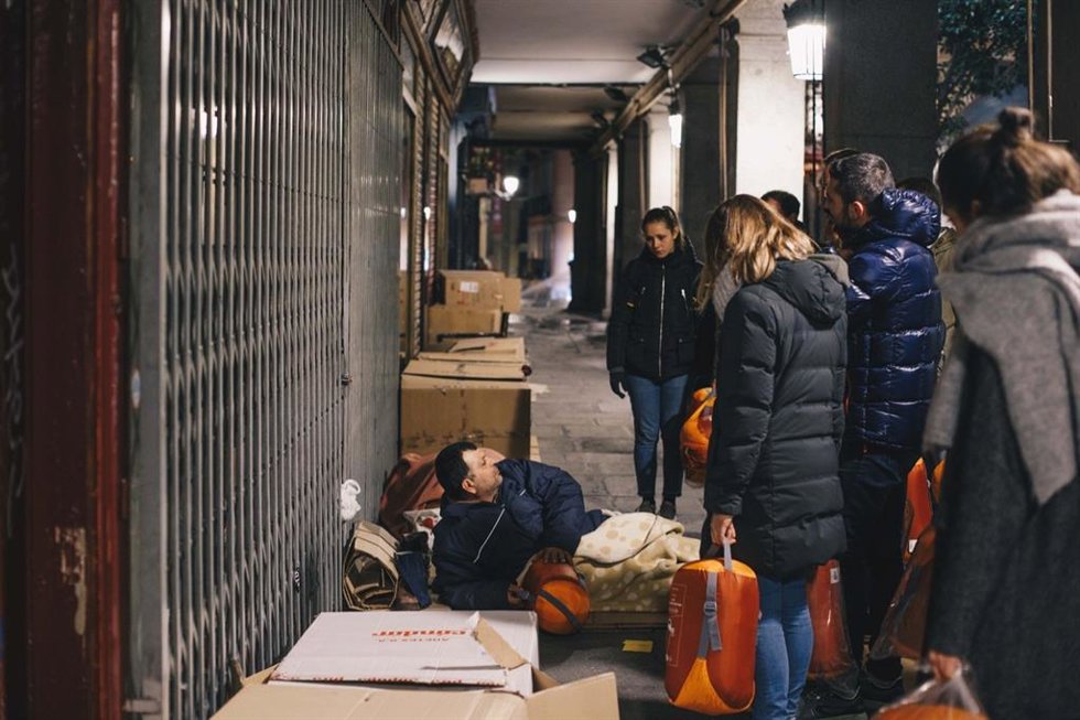 Voluntarios entregan material de abrigo a un hombre que duerme en la calle.