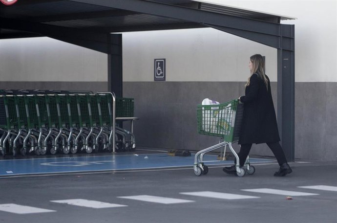 Archivo - Una mujer sale de un supermercado con un carro de la compra