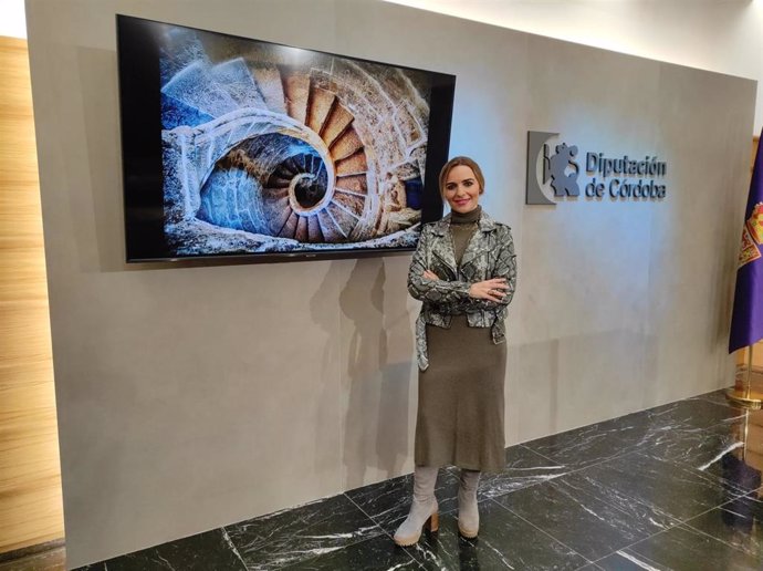 La delegada de Turismo y vicepresidenta del Patronato Provincial de Turismo de la Diputación, Narci Ruiz,  junto a la fotografía de la escalera de piedra en espiral de las Carnicerías Reales de Priego de Córdoba.