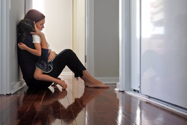 Archivo - Mujer sentada en el suelo del pasillo abrazando a su hija. Depresión, dolor, trauma.