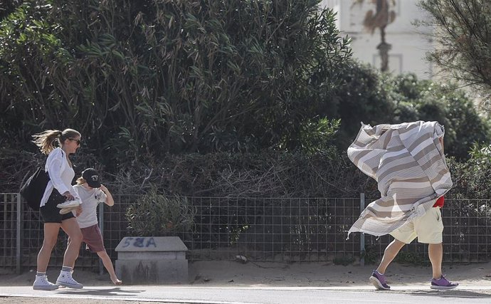 Una persona se refugia con un pañuelo del viento en el paseo de la playa de la Malvarrosa en imagen de archivo