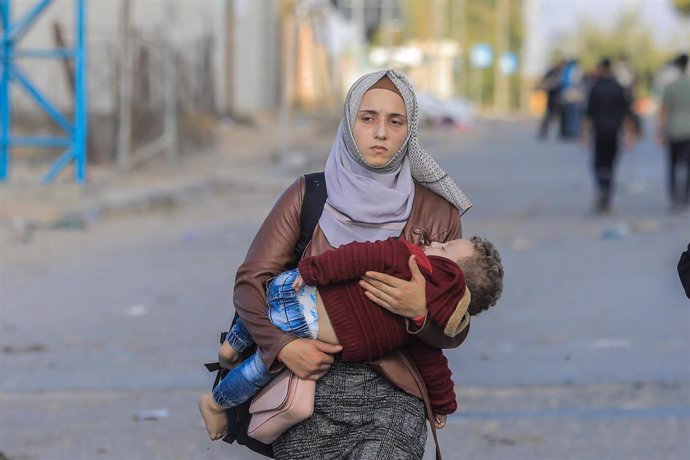 Una mujer porta a su hijo escapando de la Franja de Gaza