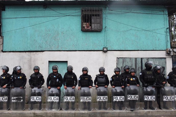 Archivo - Una mujer observa la situación desde su ventana mientras agentes de la Policía de Guatemala se paran frente a su casa durante las protestas en Guatemala