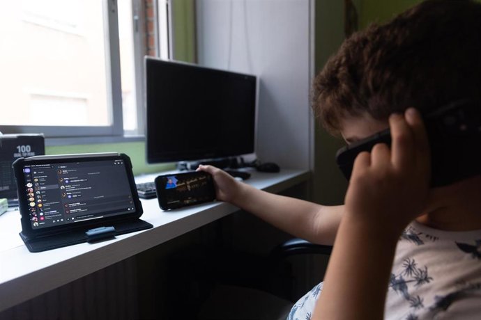 Archivo - Un niño usa el teléfono móvil y una tablet