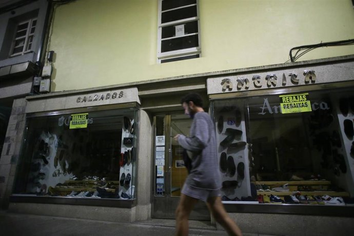 Archivo - Una persona camina al lado de una tienda de ropa sin iluminación, a 10 de agosto de 2022, en Lugo, Galicia (España). Hoy entran en vigor las primeras medidas del Plan de medidas de Ahorro y Eficiencia Energética de la Administración General de