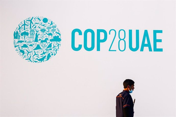 Un trabajador camina junto al logo de la COP28.