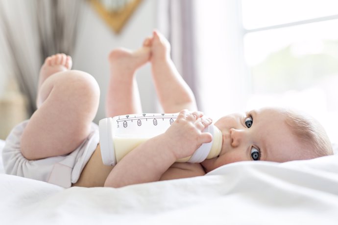 Archivo - Bebe leche acostado en cama. Pañal, bebé