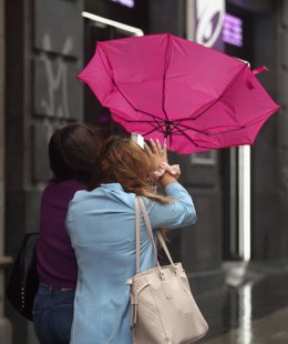 Archivo - Dos mujeres intentan controlar su paraguas ante el fuerte viento.