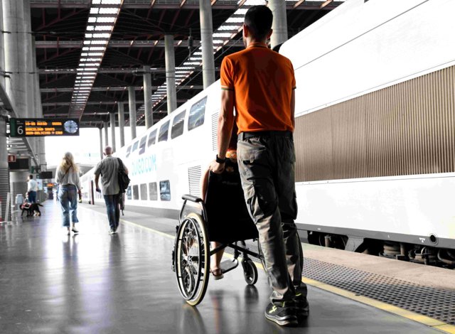 Un trabajador de Adif presta asistencia a una persona con discapacidad