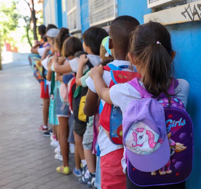 Archivo - Varios niños hacen fila con sus mochilas antes de entrar en un centro escolar, foto de recurso