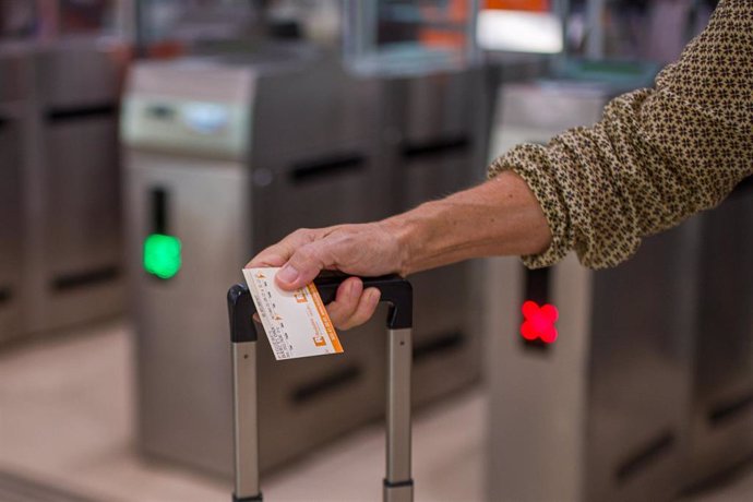 Archivo - Una viajera sostiene un billete tras cruzar los tornos de la estación de Sants de Barcelona.