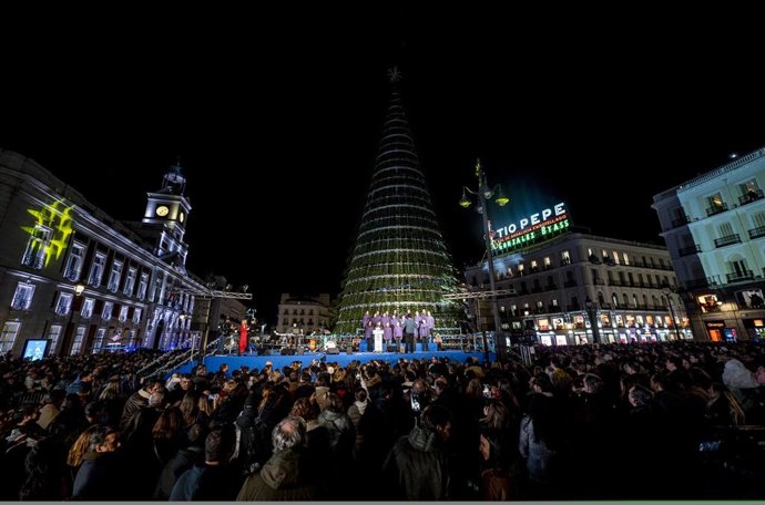 Cientos de personas asisten a la actuación de un coro, durante el encendido de luces de navidad, en la Puerta del Sol