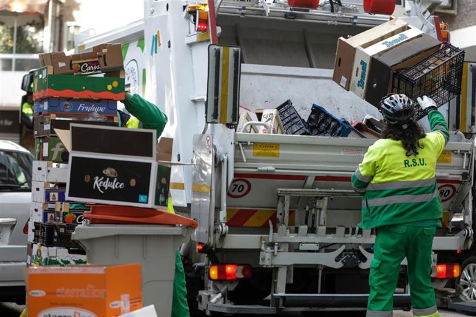 Archivo - Un operario de recogida de residuos protegidos con mascarilla coloca cajas de cartón y de plástico en la trituradora de un camión de basura  