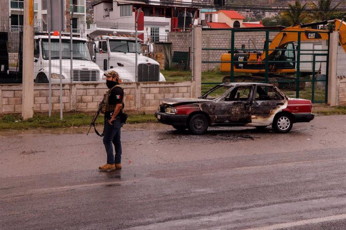 Archivo - Agente de la Policía de México junto a un coche quemado