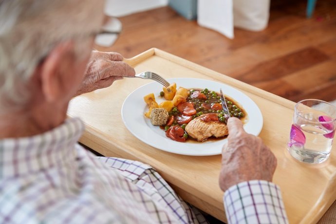 Archivo - Over shoulder view of senior man eating dinner at home