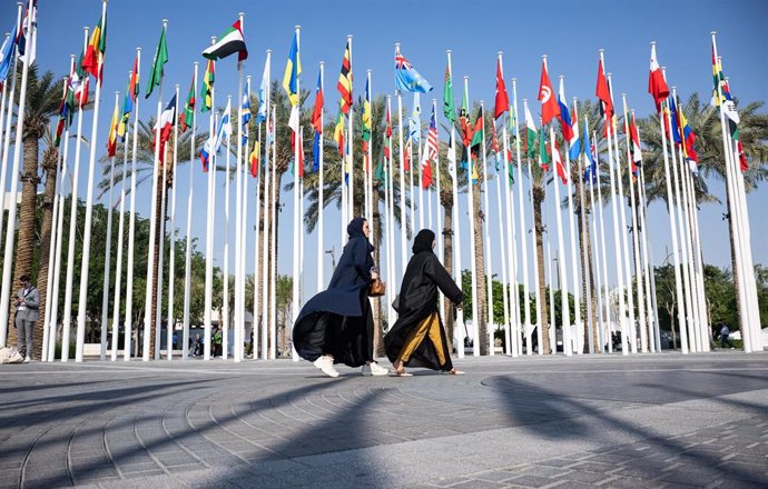 Dos mujeres pasean frente a banderas durante la celebración de la Conferencia de Naciones Unidas sobre Cambio Climático (COP28)