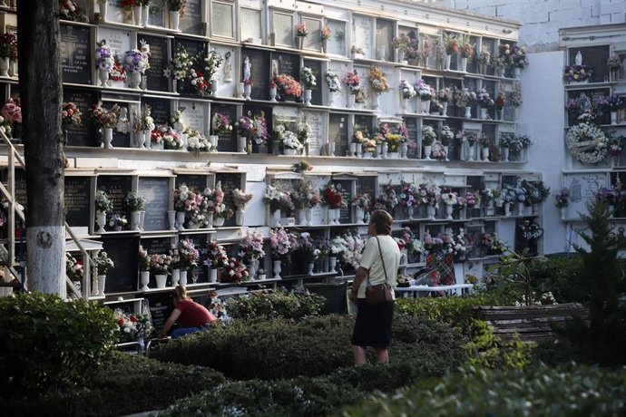 Archivo - Una mujer lleva flores a un difunto en un cementerio de Málaga.