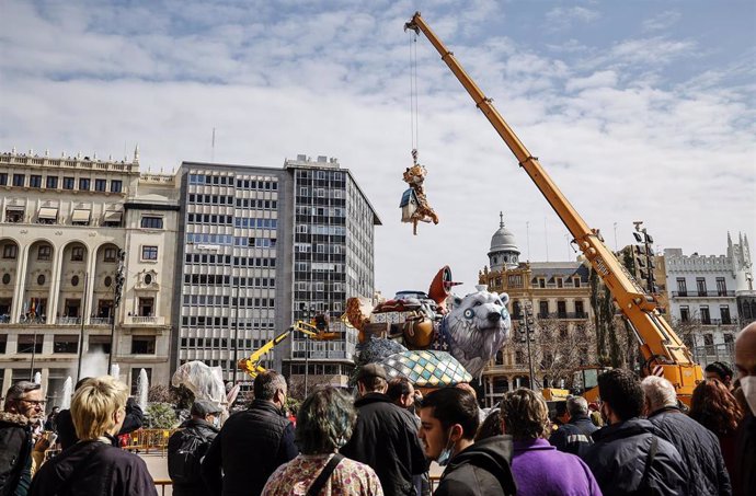 Archivo - Varias personas observan como una grúa monta la falla del Ayuntamiento para la fiesta de las Fallas 2022