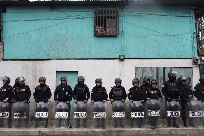 Archivo - Una mujer observa la situación desde su ventana mientras agentes de la Policía de Guatemala se paran frente a su casa durante protestas