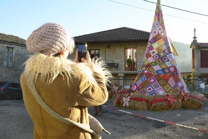 Una persona toma una fotografía frente al árbol de Navidad hecho con ganchillo, a 18 de diciembre de 2023, en Ousende, Paderne, Ourense, Galicia (España). El pueblo cuenta con adornos artesanales de todo tipo realizados por el colectivo vecinal. 