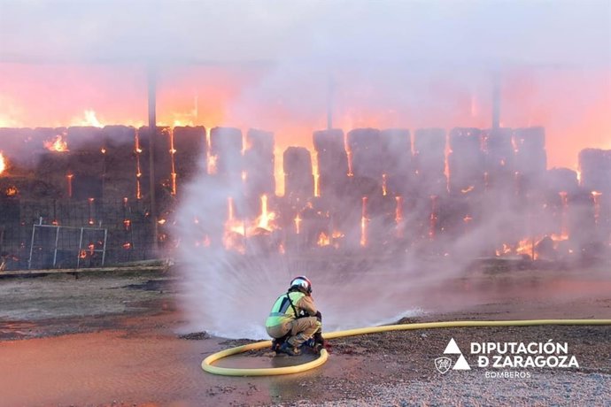 Un bombero de la DPZ participa en la extinción de un incendio de una nave de almacenaje de alfalfa.
