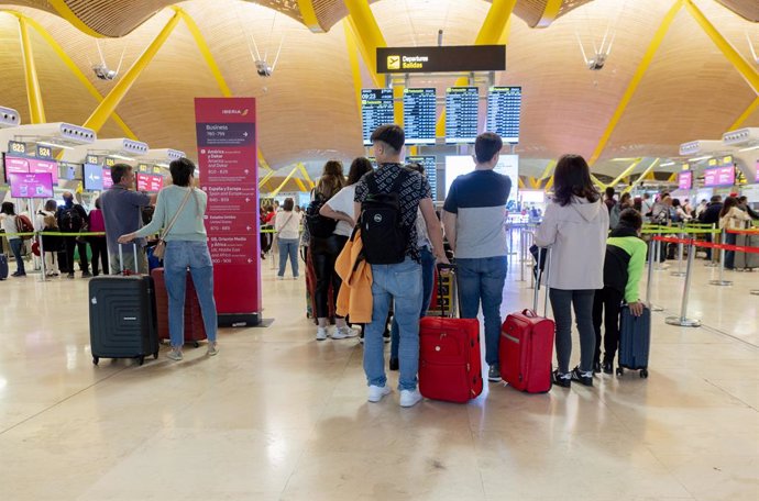 Archivo - Un grupo de personas frente al panel del orden de vuelos en la terminal T4 del aeropuerto de Adolfo Suárez-Madrid Barajas.