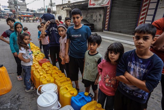Archivo - Niños palestinos hacen cola en Rafá para poder llenar bidones con agua potable.