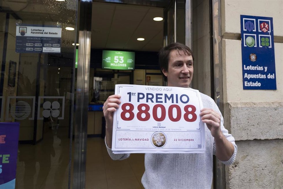 Un agraciado posa con su décimo del Primer Premio del Sorteo Extraordinario de Lotería de Navidad 2023 correspondiente al número 88008 en la administración donde compraron sus décimos, a 22 de diciembre de 2023, en Teruel.