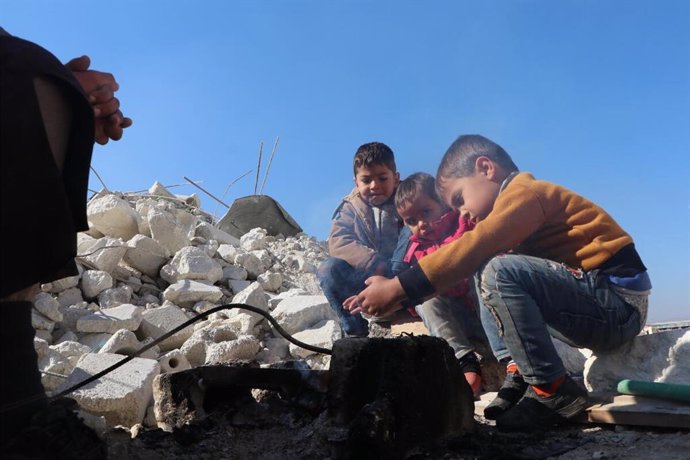 Archivo - Niños que intentan calentarse tras la destrucción de sus viviendas por los terremotos en Siria.