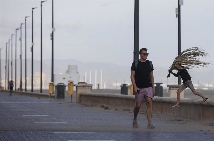 Archivo - Un hombre anda por el paseo de una playa valenciana con rachas de viento en imagen de archivo