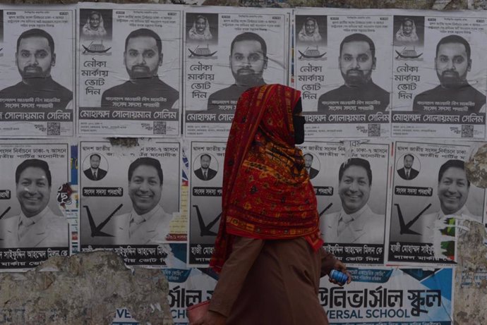 Una mujer pasa mientras se colocan carteles de campaña electoral en una pared cerca de una calle antes de las elecciones generales en Daca, Bangladesh