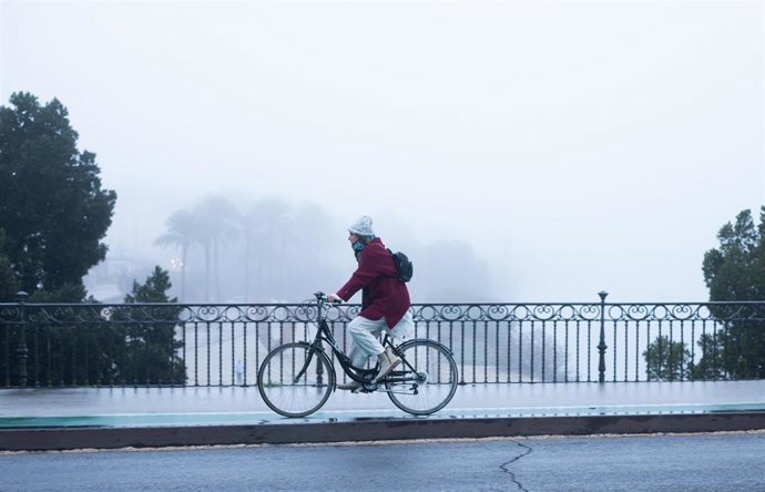 Archivo - Una ciclista se protege del frío con gorro y guantes en el Puente de Triana, en Sevilla (Andalucía, España).
