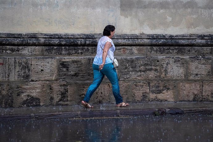 Archivo - Una mujer anda por la calle bajo la lluvia.