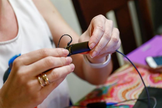 Archivo - Una mujer usuaria de un implante coclear coloca un adaptador para el audífono para hablar a través de una videollamada.