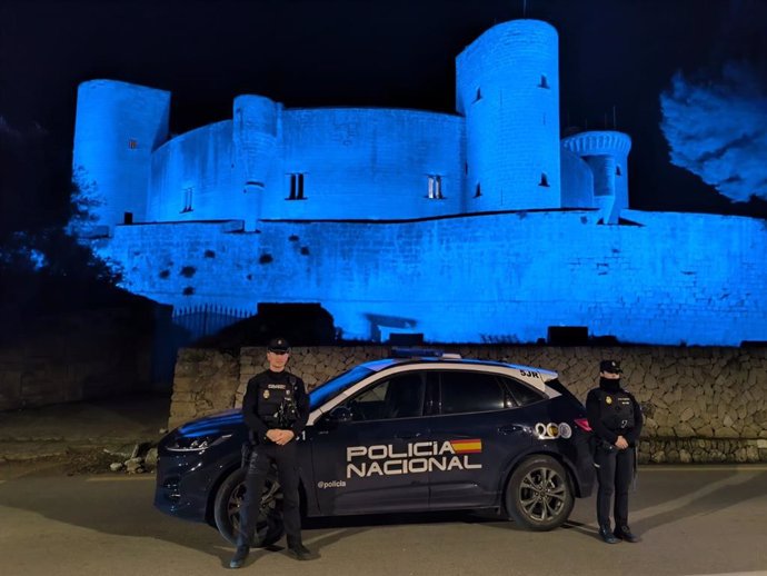 Agentes de la Policía Nacional, junto a un vehículo policial, y, tras ellos, el Castillo de Bellver, teñido de azul por el Bicentenario del Cuerpo