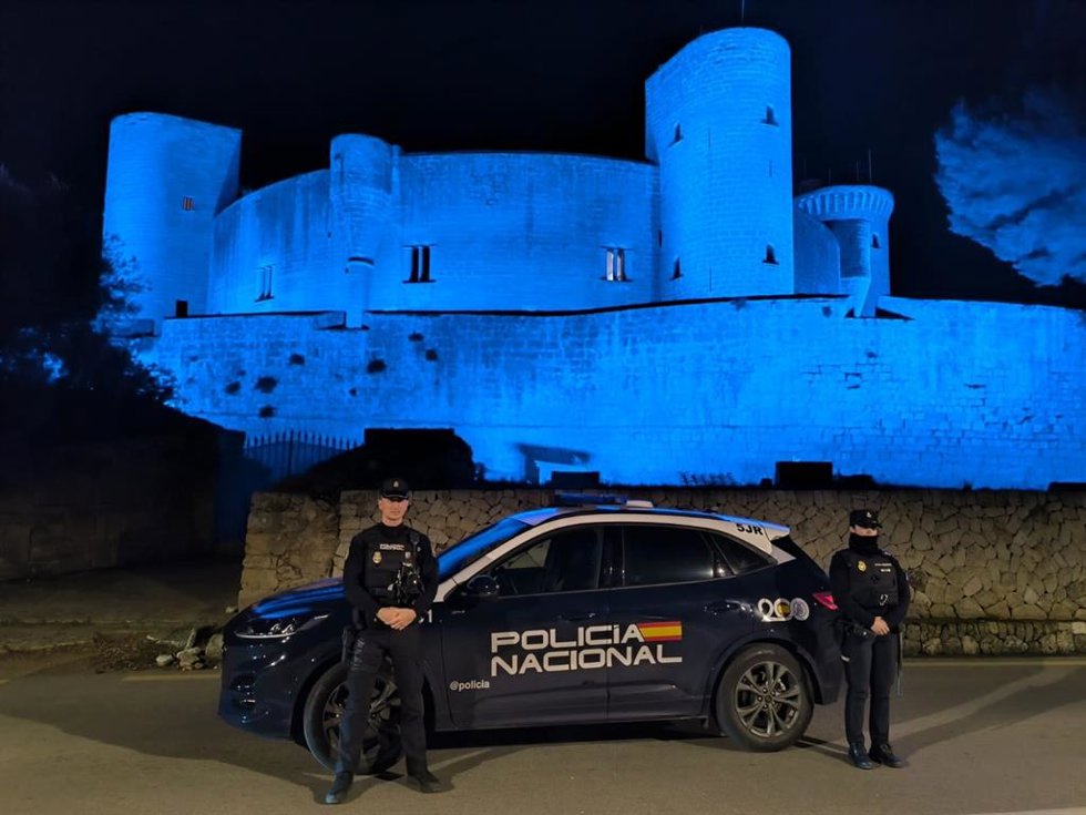 Agentes de la Policía Nacional, junto a un vehículo policial, y, tras ellos, el Castillo de Bellver, teñido de azul por el Bicentenario del Cuerpo