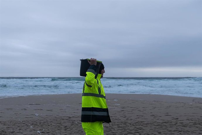Un hombre carga un cubo lleno de pellets, en la playa Do Dique, a 13 de enero de 2024, en Queiruga, A Coruña, Galicia (España). La conocida ya como la marea blanca, se prevé que proceda de los seis contenedores del buque Toconao que cayeron al mar en 